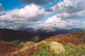 Hills w shadows from big clouds on  blue sky, green grass and dried fern + stone in foregrd