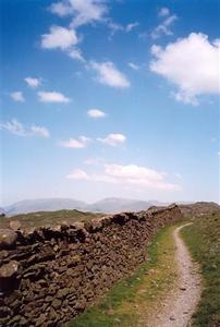 Stone wall and path on top of hill, blue sky with a few light clouds