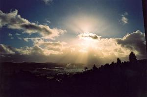 Sun behind cloud, beams dark landscape and sky