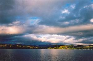 Pink light colouring heavy grey clouds above grey lake