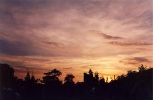 Setting sun behind school tower and wooded horizon