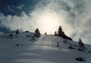 Sun behind clouds and snow covered hill