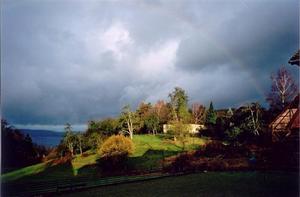 Sun light on hill thru grey-blue sky over hill, faint rainbow